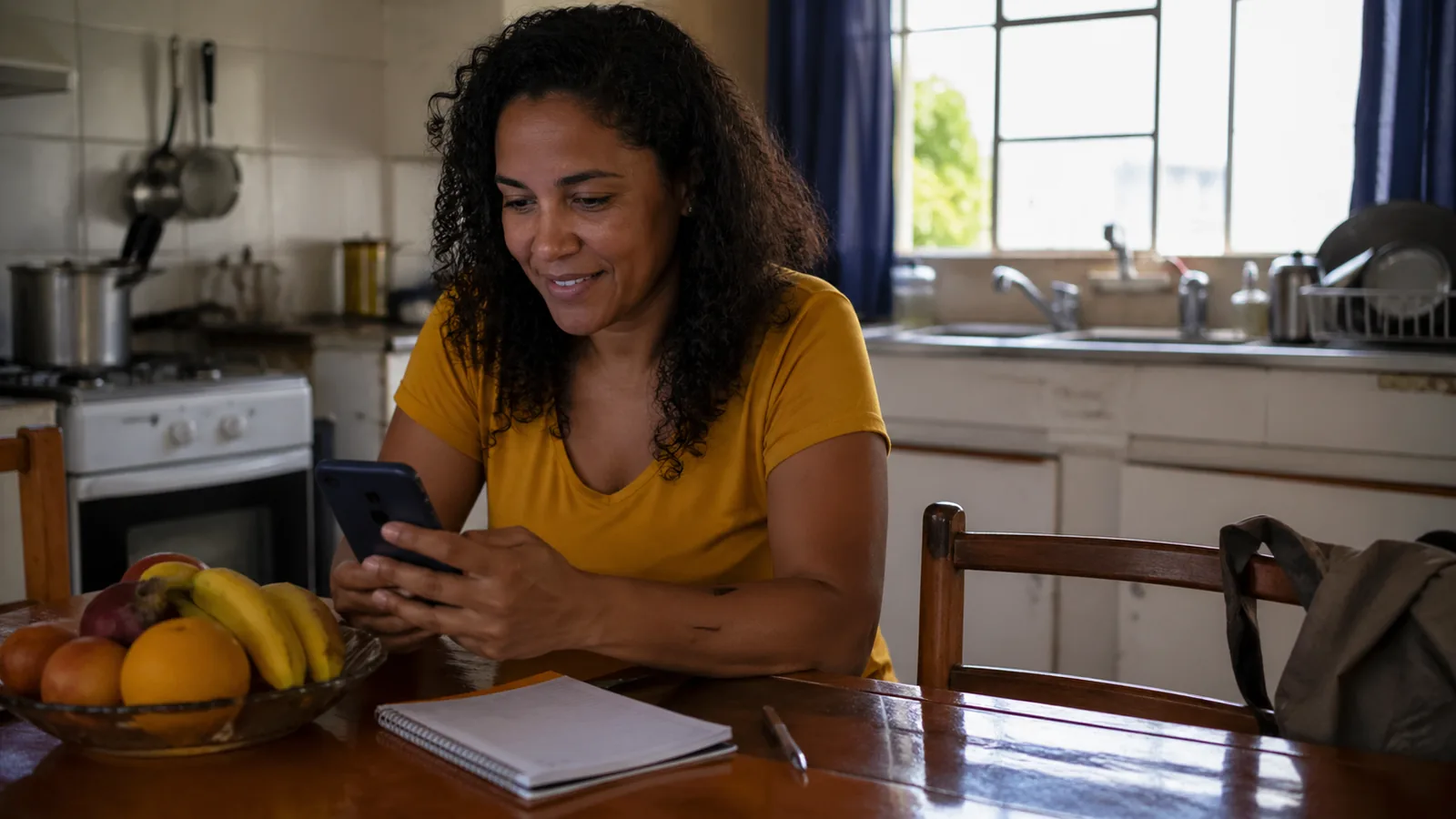 Mãe brasileira em sua cozinha conferindo benefício no celular